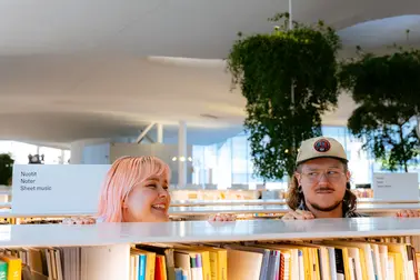 Nuori nainen ja mies hyllyjen välissä Oodi-kirjastossa.