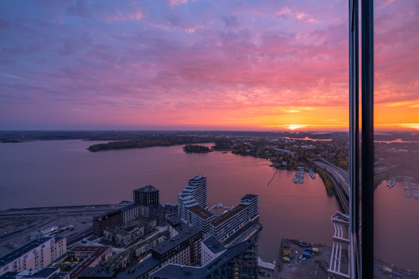 Auringonnousu Helsingissä. Kuva on otettu kerrostalosta ja ikkunasta näkyy silta ja toimistoja sekä merta.