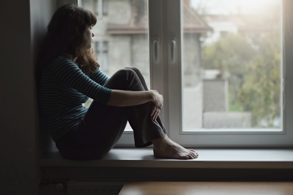 Nuori nainen istuu yksin ikkunassa ja katsoo ulos.