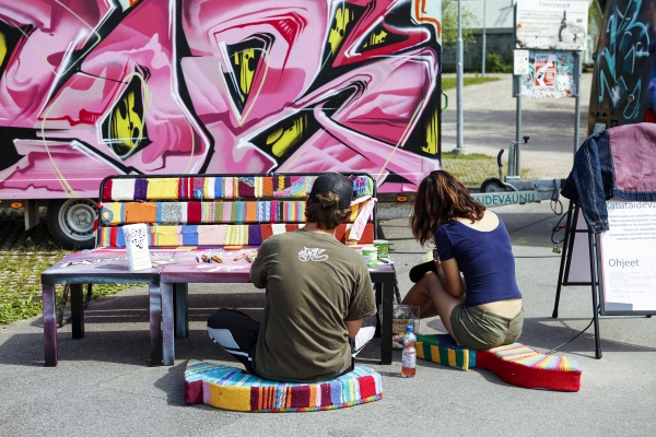 Nuori mies ja nainen istualtaan ja selin graffitin edessä Pihlajamäen nuorisopuistossa.