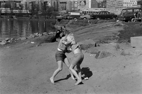 Kaksi poikaa painimassa rystypainia rantahietikolla Siltasaarenkärjessä. Taustalla Linjojen kerrostaloja. Kevät 1970.
